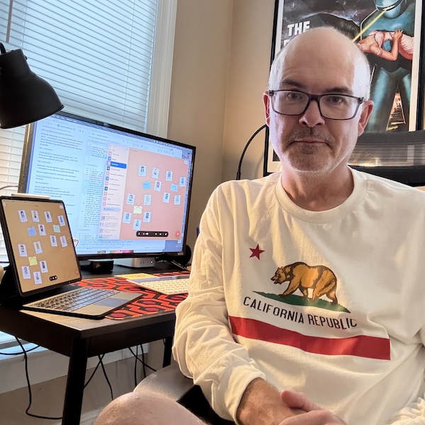 Chris Ainsworth at his desk, with Crazy Wall open on a Mac and an iPad